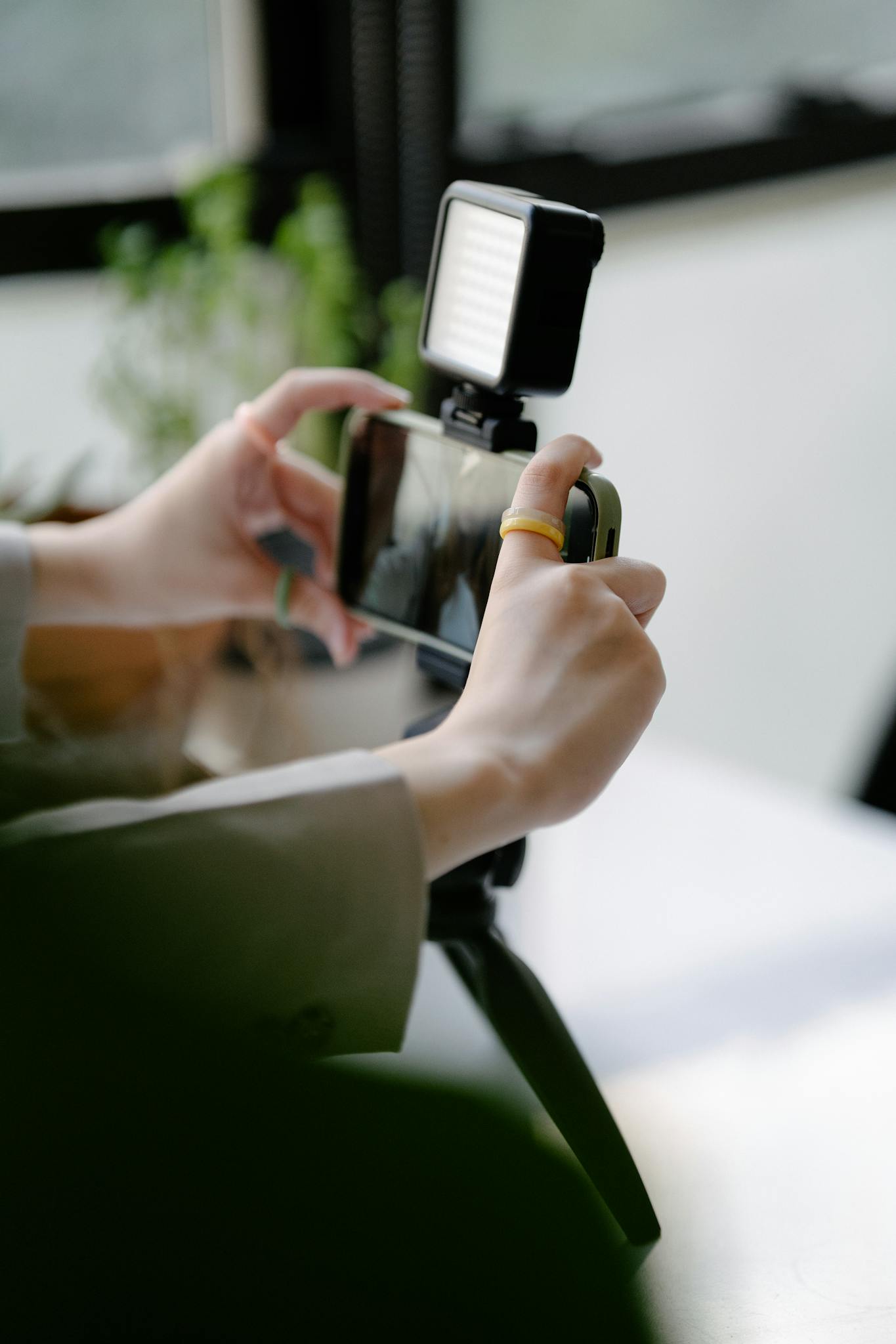 Close-up of hands operating smartphone on a tripod with LED light indoors.
