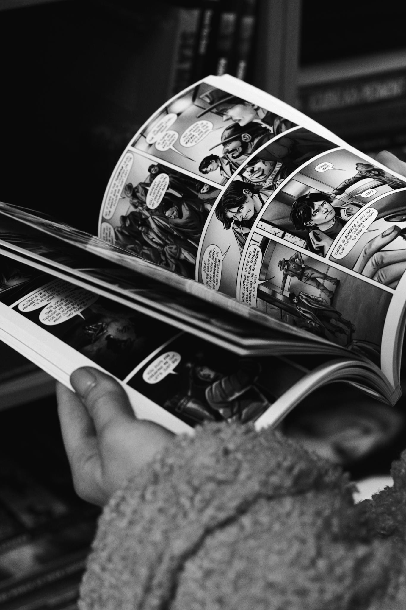 Close-up of hands reading a black and white comic book, focus on the comic panels.